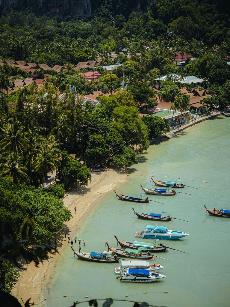 Serene aerial shot of longtail boats along Krabi beach, capturing lush greenery and coastal village.