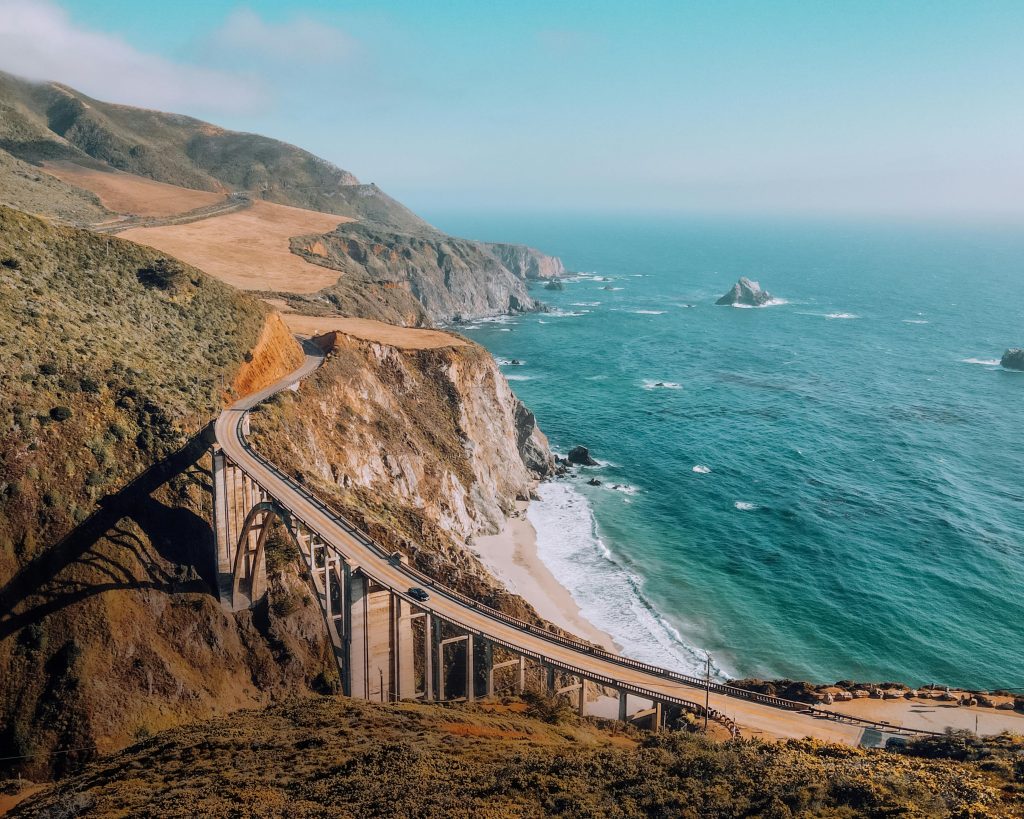 Stunning aerial view of Bixby Creek Bridge on California's rugged coastline with turquoise ocean and cliffs.