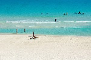 Sunbathers and swimmers enjoy a sunny day at a pristine white sand beach.